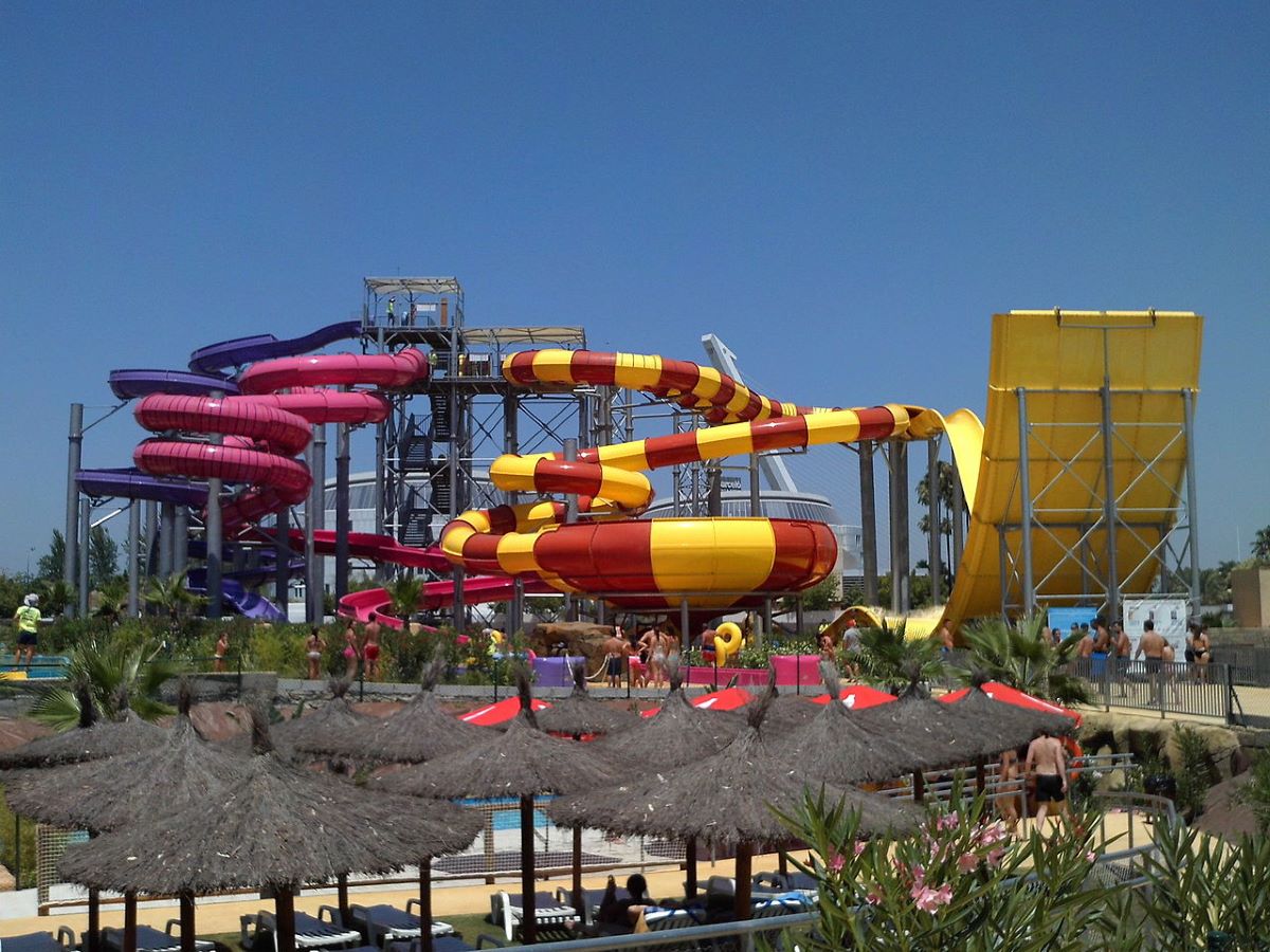 Slides at Agua Mágica in Seville in the background as patrons relax under shaded cabanas. 