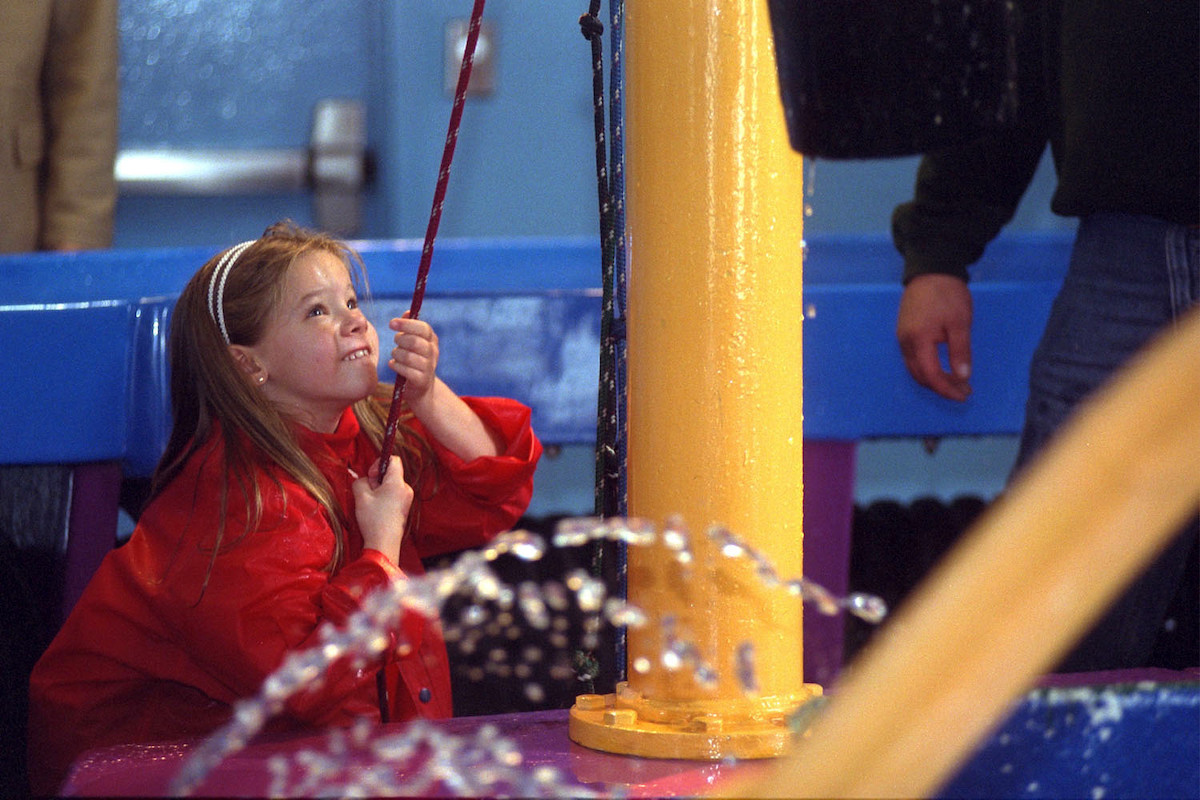 One of the best places to visit in Chicago with kids, a girl wearing a red coat tugs at a rope at the Chicago Children's Museum