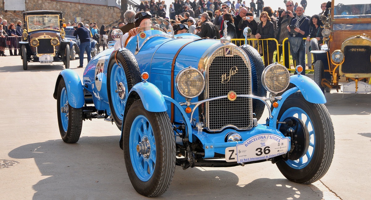 Antigue blue car rolls into town with a crowd of awaiting spectators