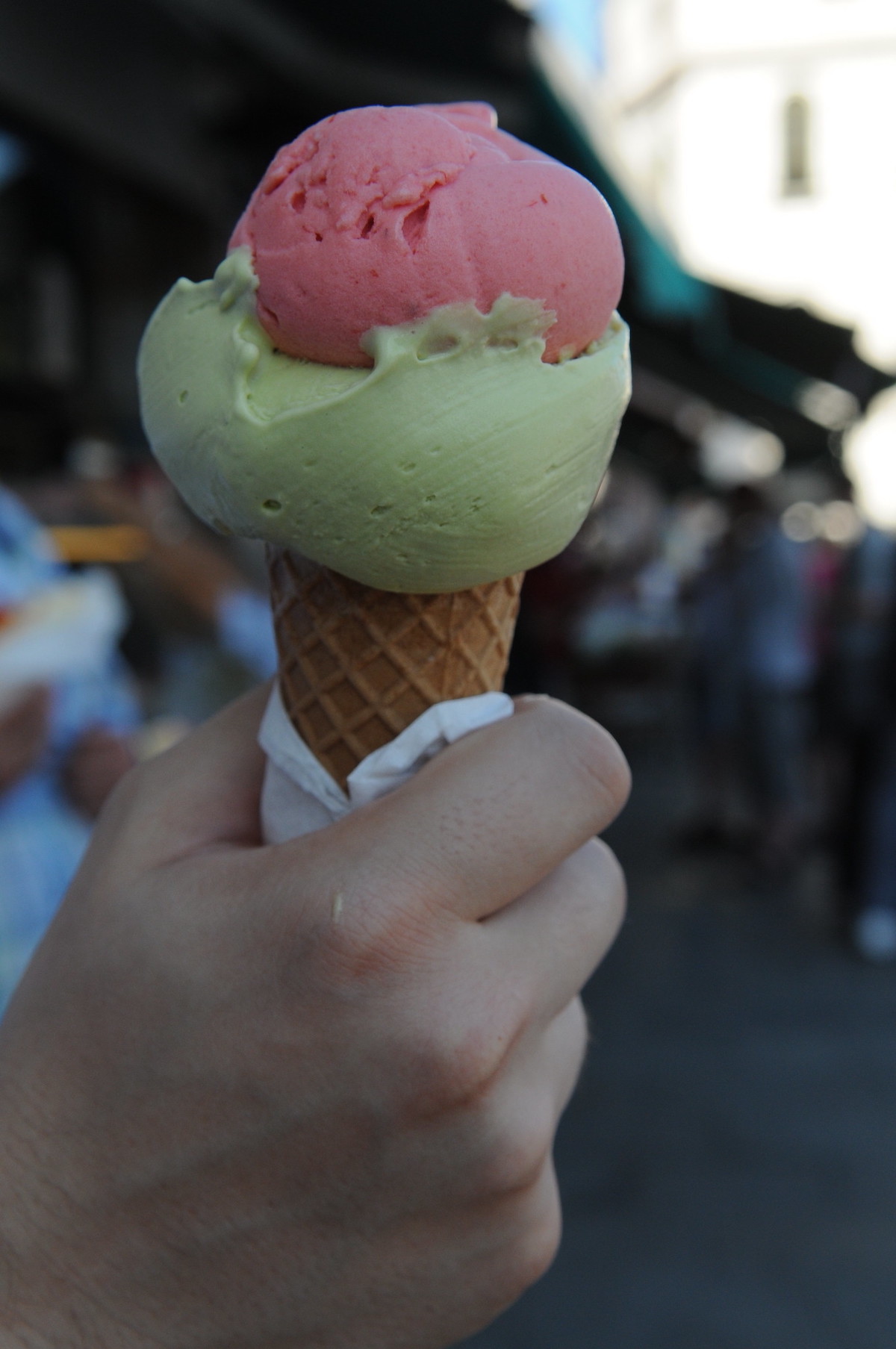 close up of someone holding a cone with two scoops of gelato, one light green and one pink