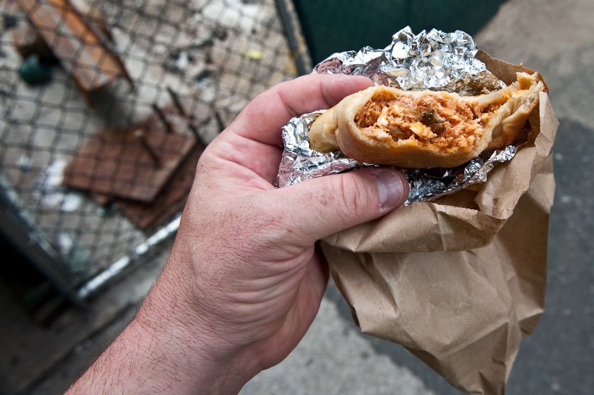 A person holding an empanada that has been bitten into. 