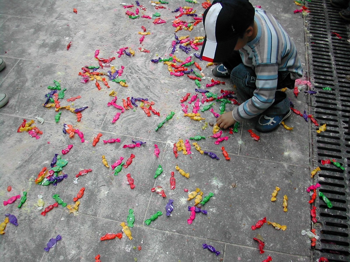 Small child crouches on the ground to collect multicolored pieces of wrapped candy