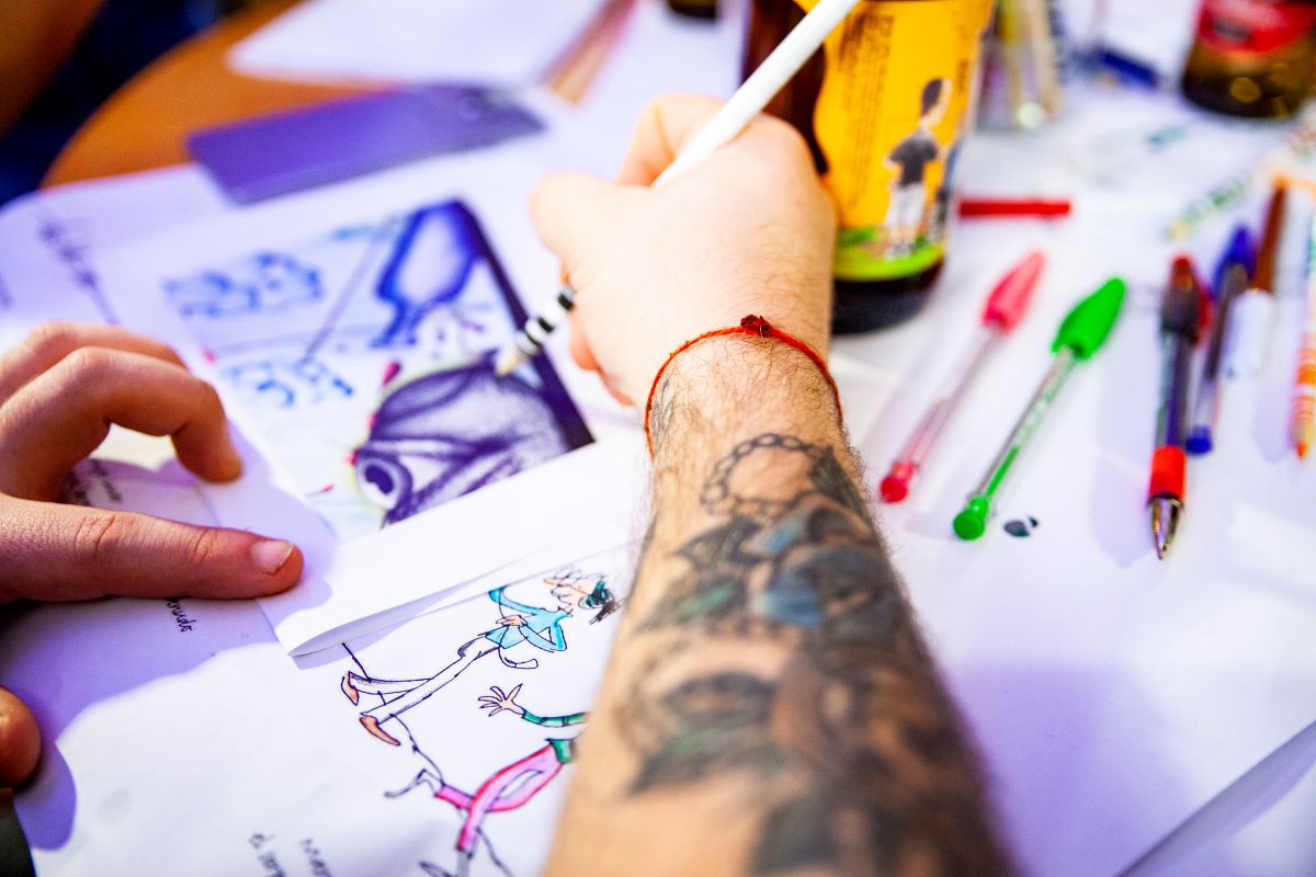 A tattooed man drawing at a drink and draw event at a wine shop in Lisbon. 