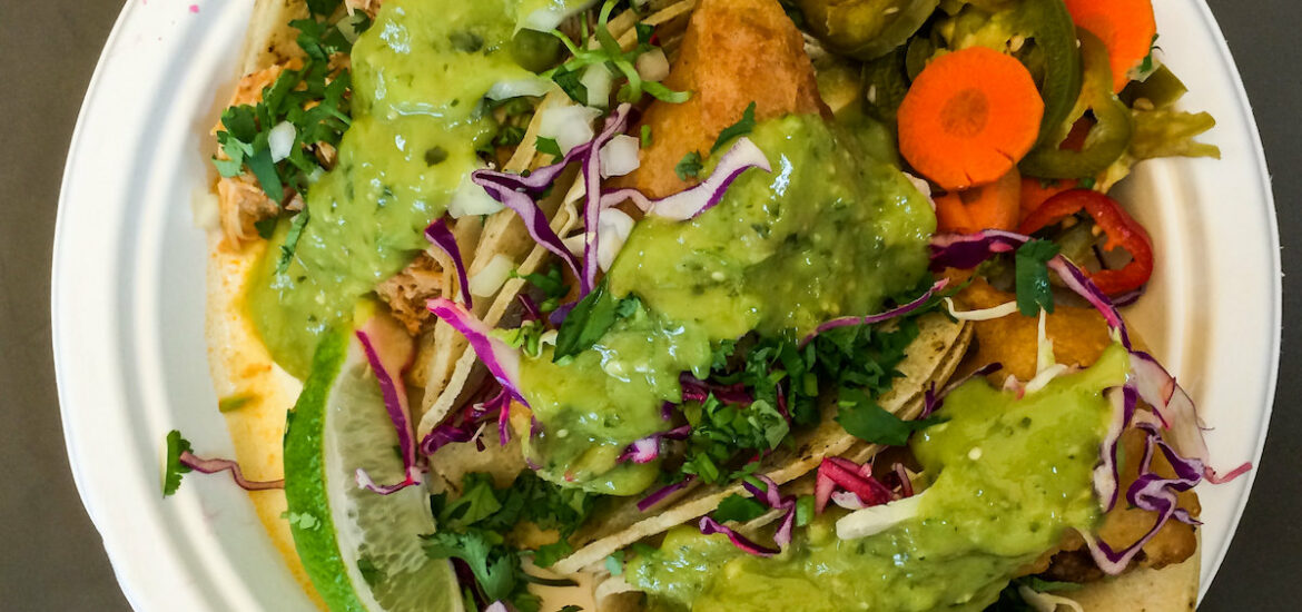 a paper plate loaded with three tacos covered in guacamole