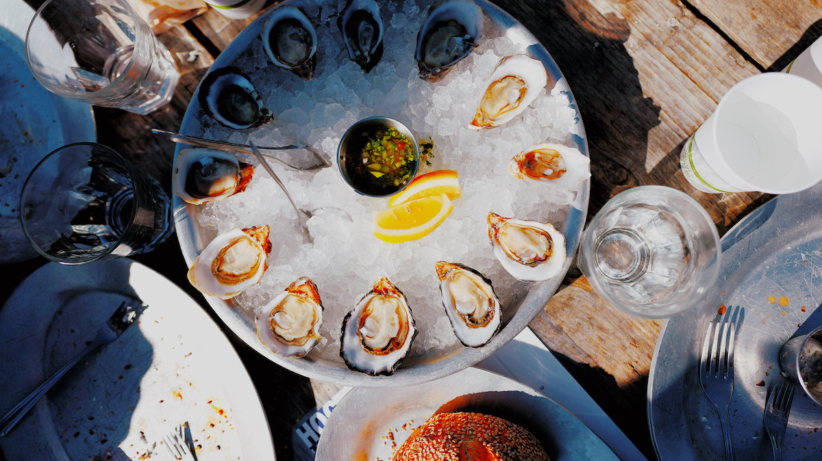 An overhead shot of a dining table at Hog Island Oyster Co. in San Francisco. A round tray filled with ice is topped with raw oysters on the half shell. Pacific Oysters are a food San Francisco is known for.