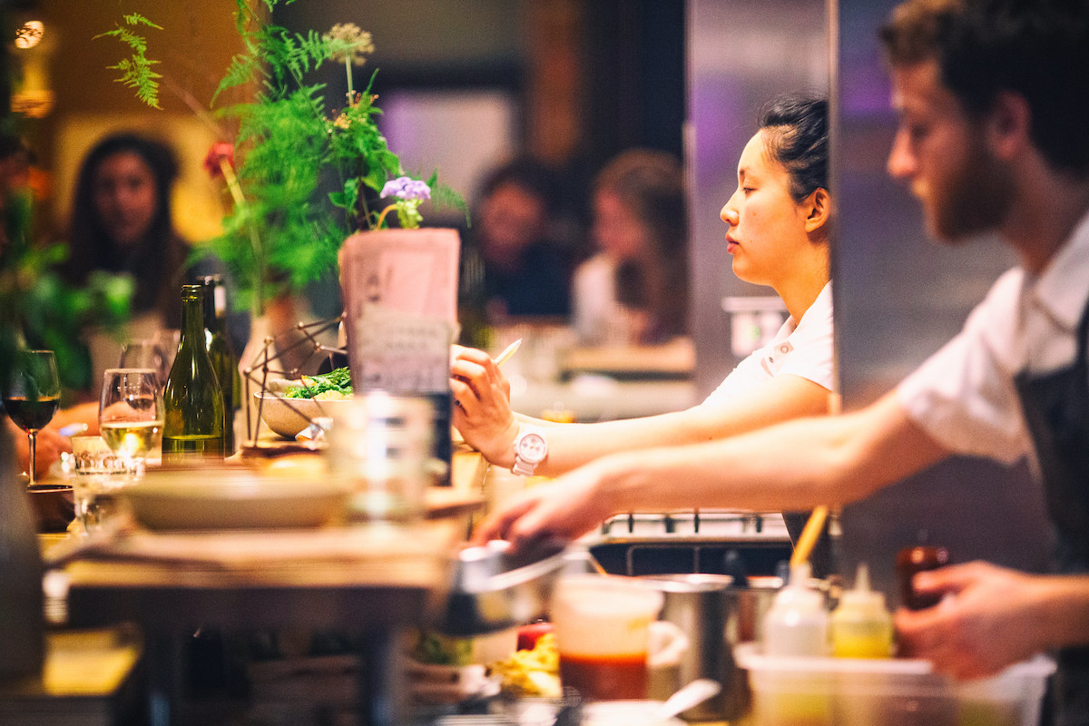 Two chefs plate dishes in front of restaurant guests