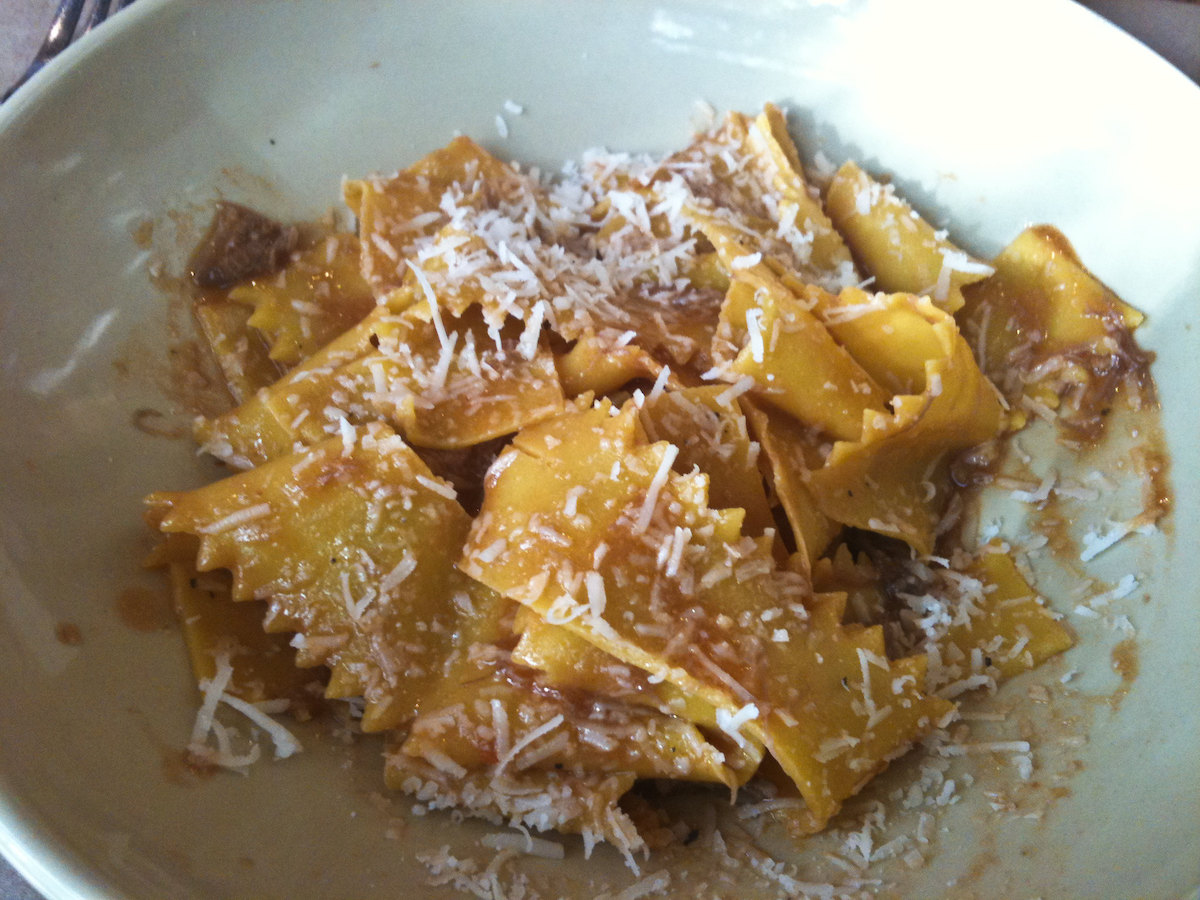 Close up of a white bowl filled with wide, flat handmade pasta pappardelle with lamb ragu and topped with grated white cheese