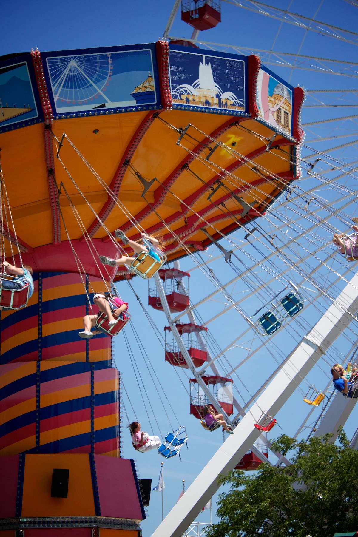 people ride a colorful swing ride with a big Ferris Wheel in the background at Navy Pier in Chicago, a great place to go with kids