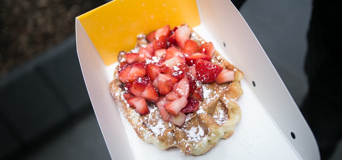 A takeout container with one waffle topped with powdered sugar and strawberries