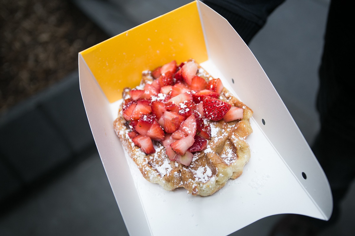 A takeout container with one waffle topped with powdered sugar and strawberries