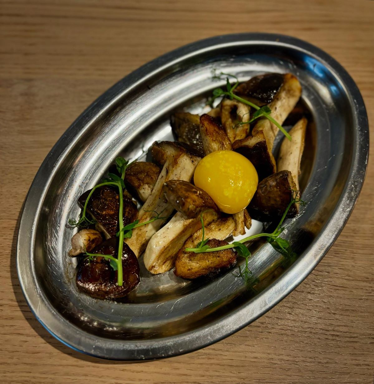 silver plate of mushrooms topped with an egg yolk