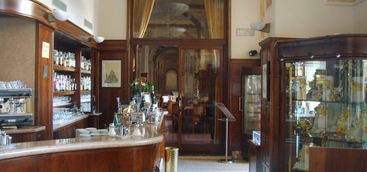 Interior of a historical cafe in Florence, Italy with a wraparound bar, dark wood details and a 1920s light fixture