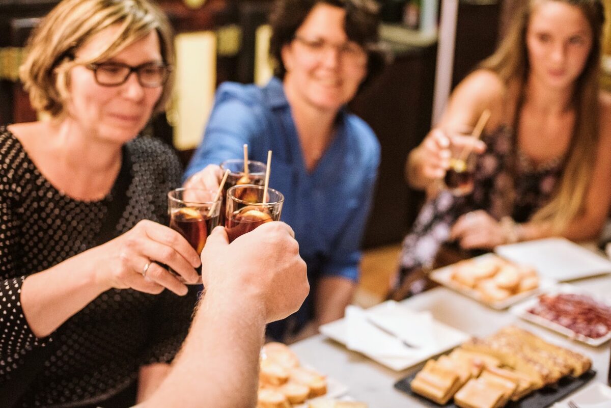 A group of people in Barcelona eating tapas and cheering with glasses of vermouth. 