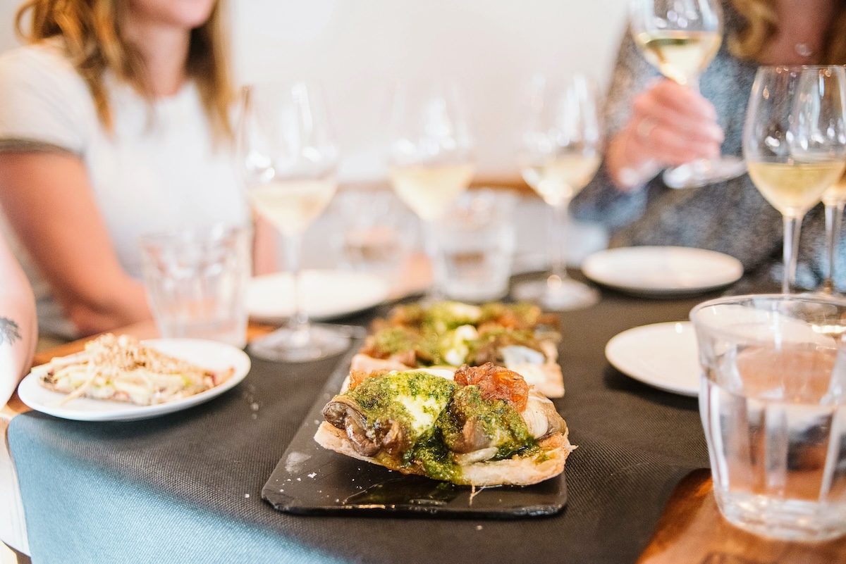 Women at at a restaurant table with a plate of food and several wine glasses