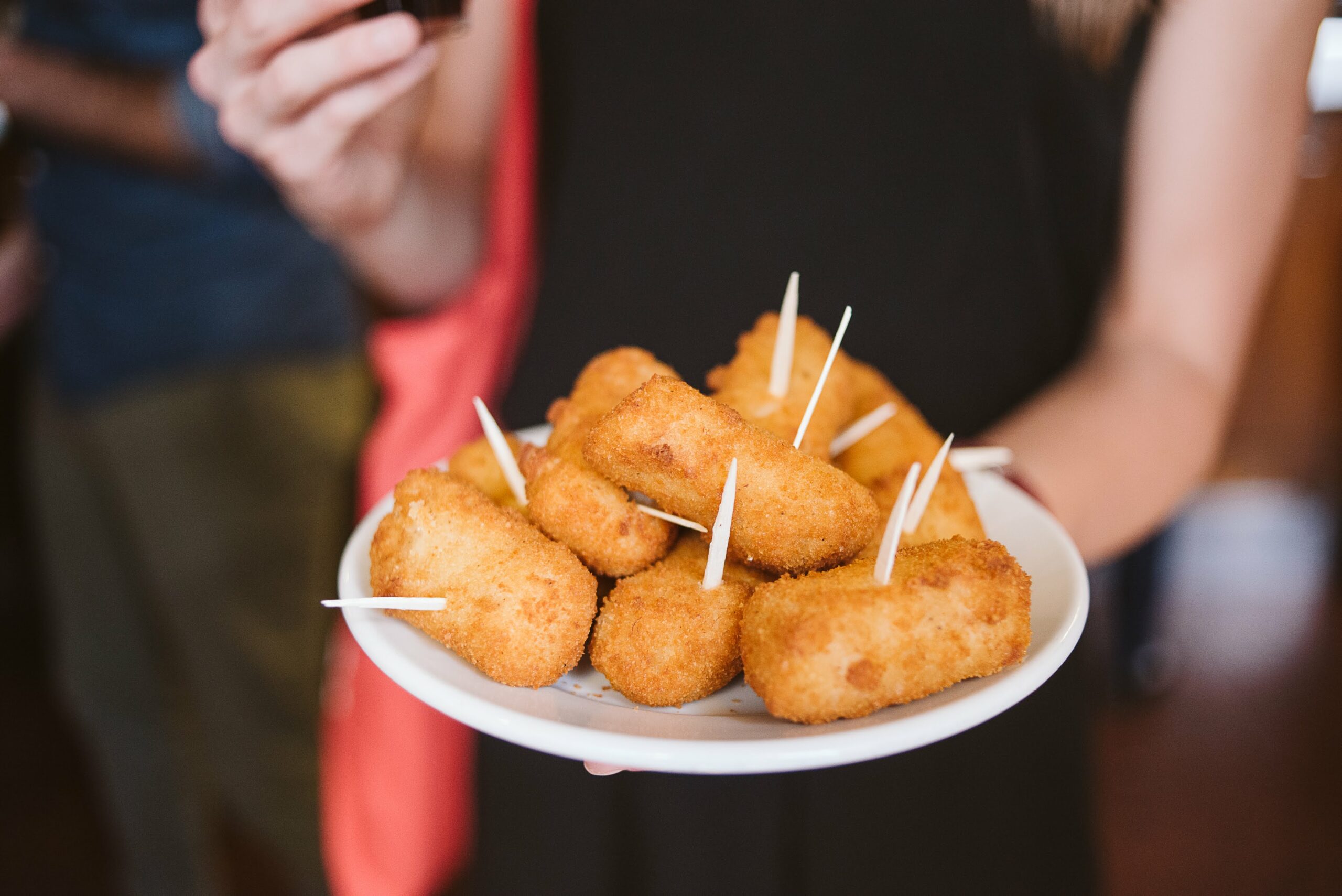 person holding a plate of croquettes with toothpicks.