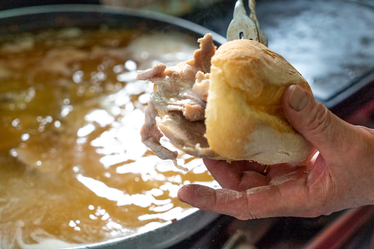 employee stuffing a bifana bun with stewed, garlicky meat