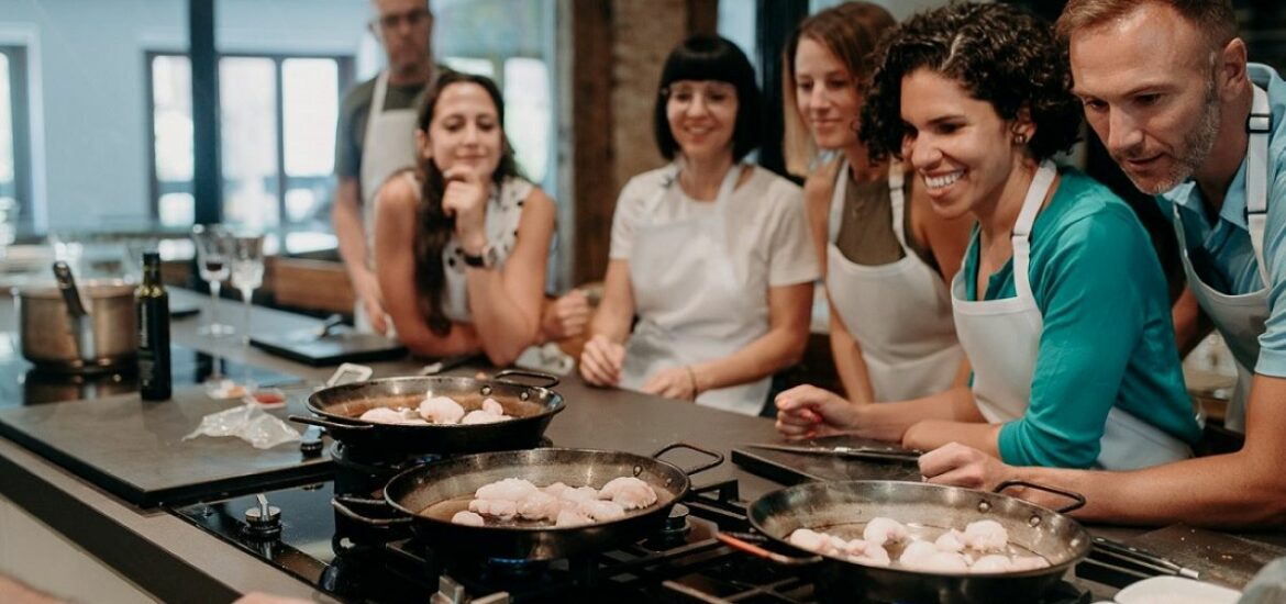 Students in a Devour cooking class look on at their paellas on the stove