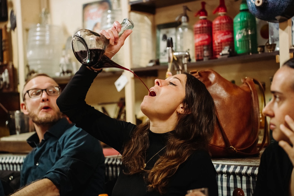 woman drinking wine from a glass decanter with a pointed spout