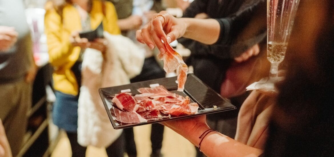 someone picking up a slice of ham off a black square plate