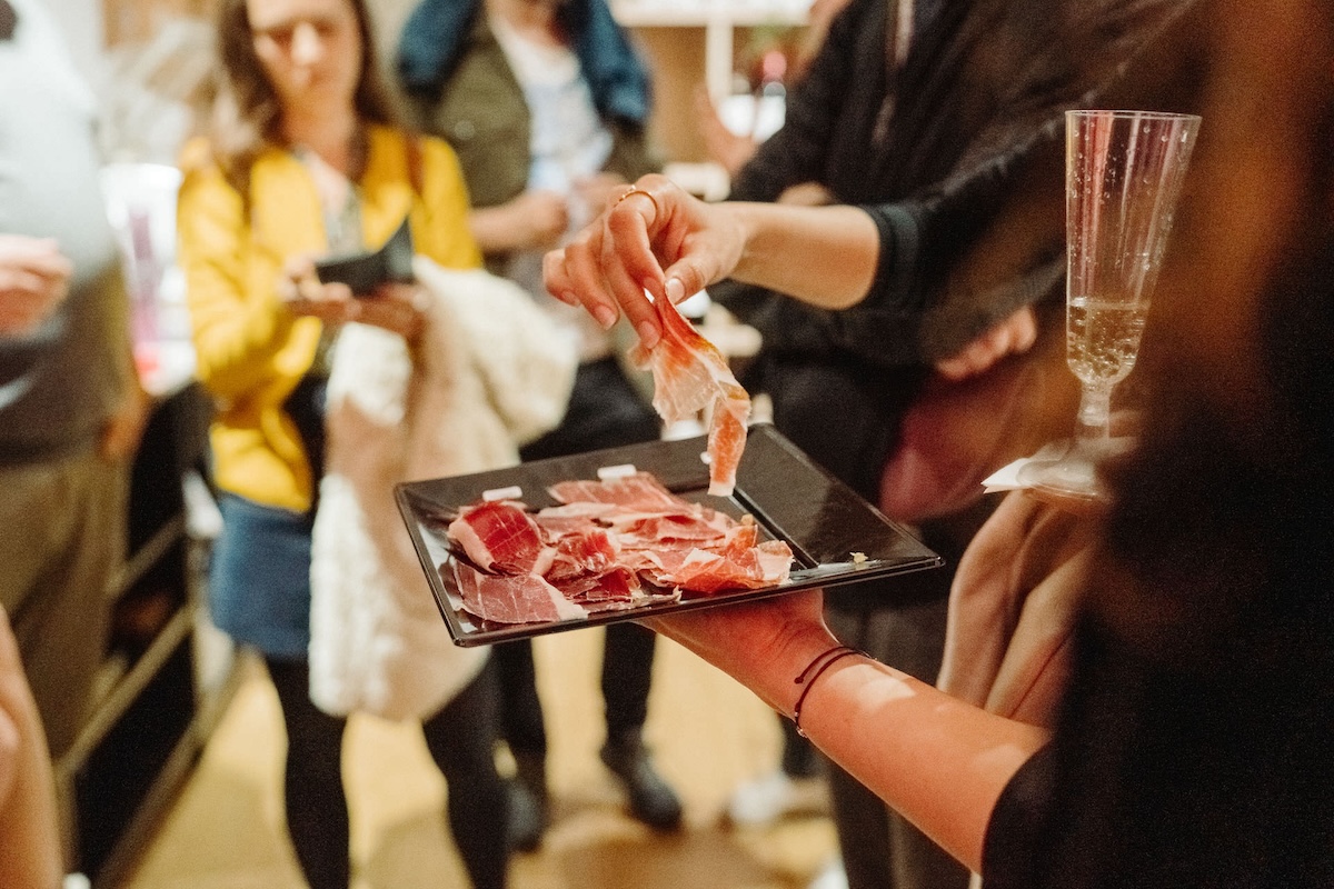 someone picking up a slice of ham off a black square plate