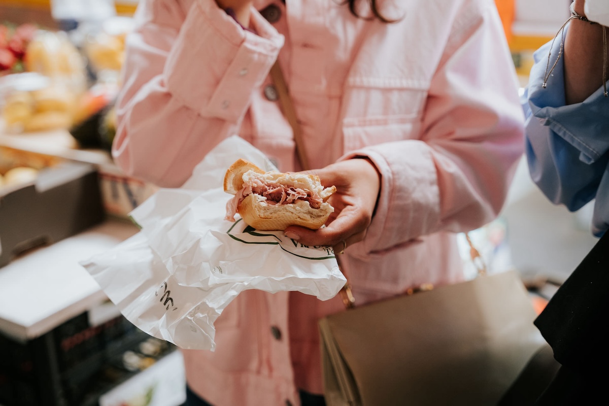 woman holding small sandwich stuffed with sliced of meat in her hand