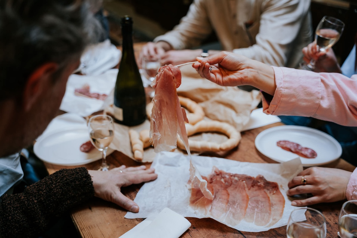 woman at a table holding up slice of ham with a fork