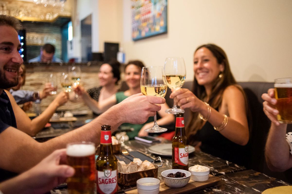 People at a restaurant in Portugal cheering wine glasses and drinking Portuguese beers.