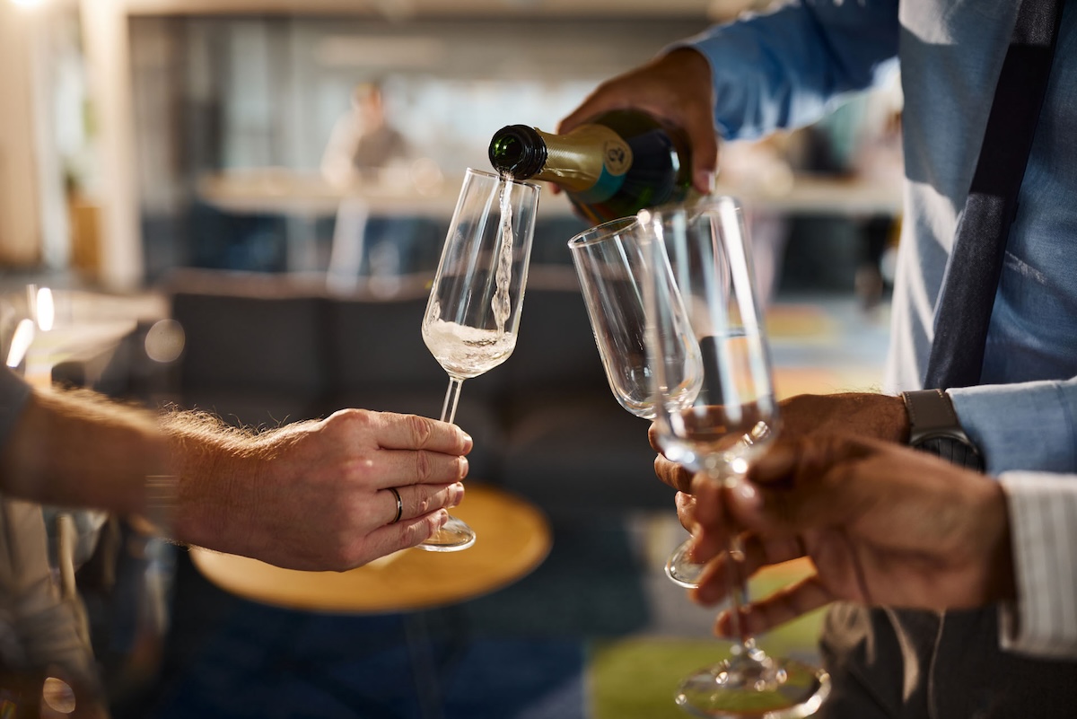 Close up of unrecognizable businessman pouring champagne to his colleagues on a party in the office.