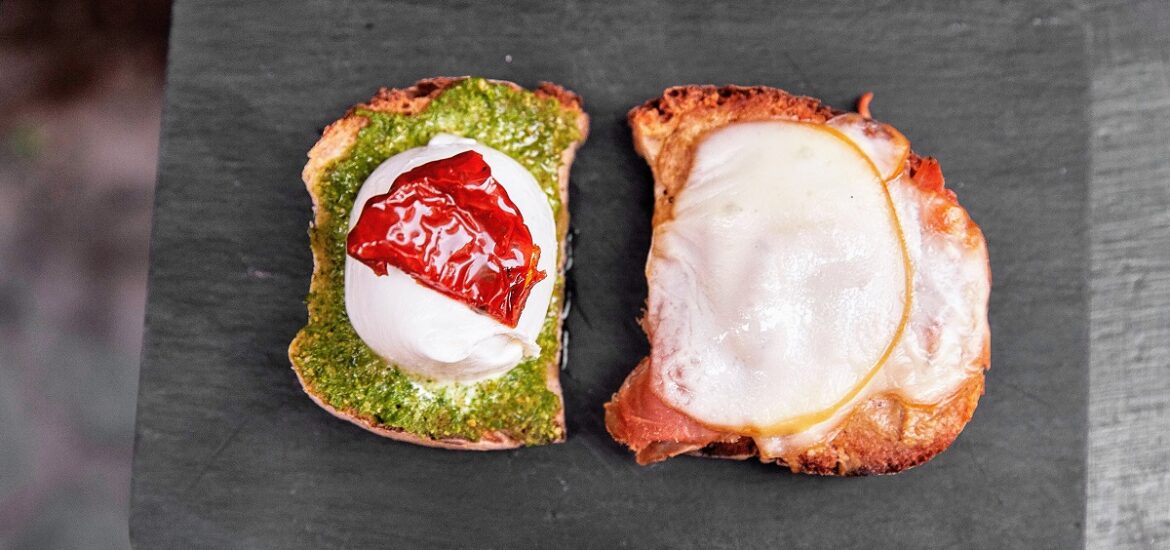 Toast of buffalo mozzarella balls on toast with pesto, tomato and some sort of meat