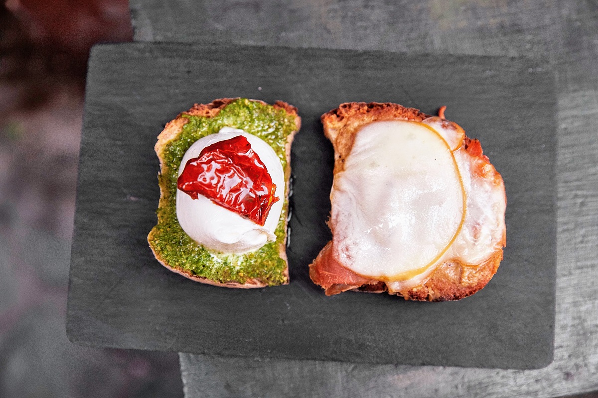 Toast of buffalo mozzarella balls on toast with pesto, tomato and some sort of meat