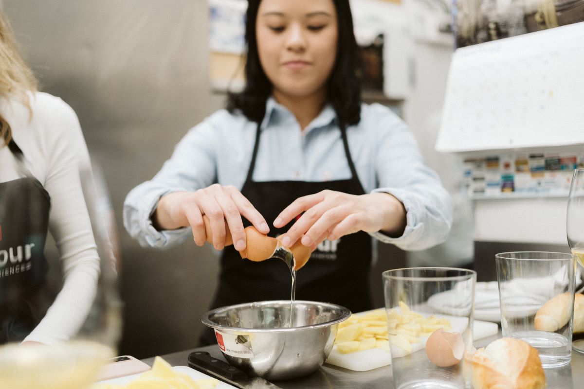 A girl cracks an egg over a bowl while preparing a recipe