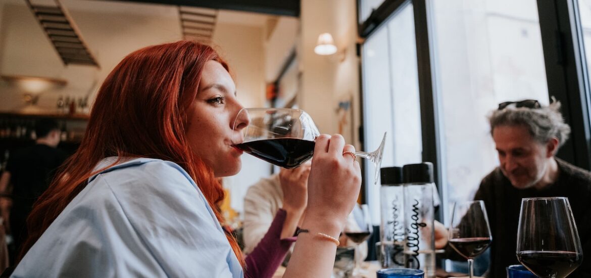 woman with auburn hair drinking from glass of red wine