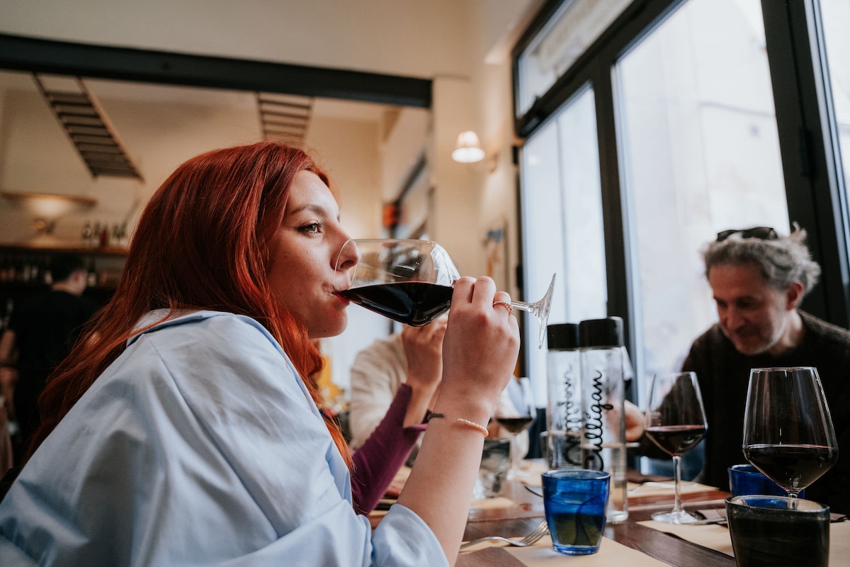 woman with auburn hair drinking from glass of red wine