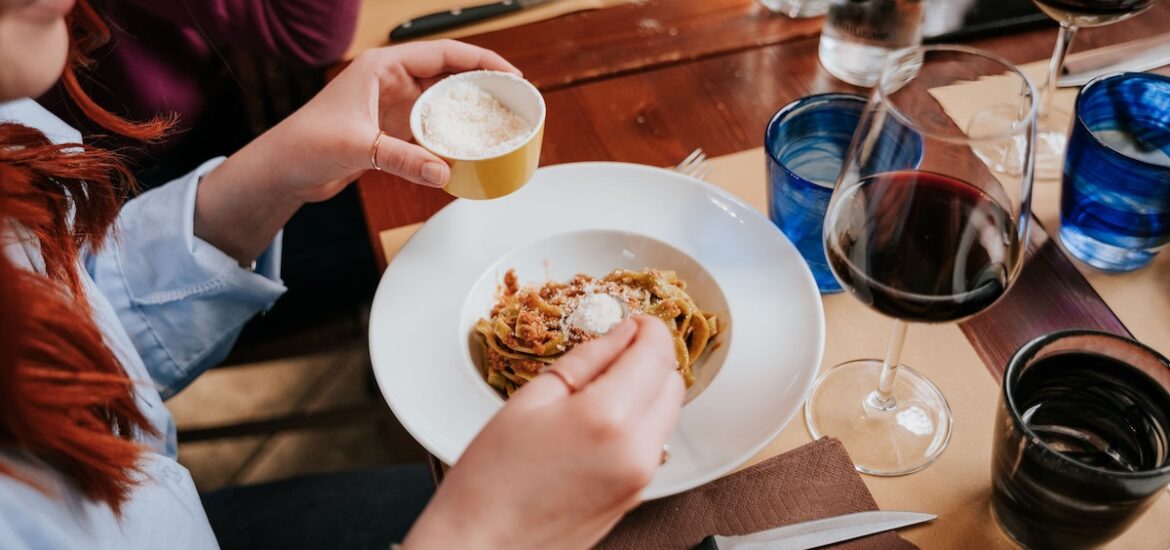 woman sprinkling parmesan cheese on plate of pasta