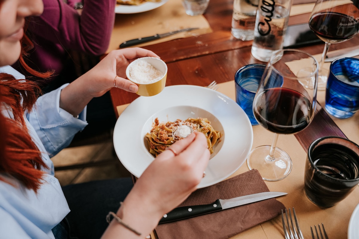 woman sprinkling parmesan cheese on plate of pasta