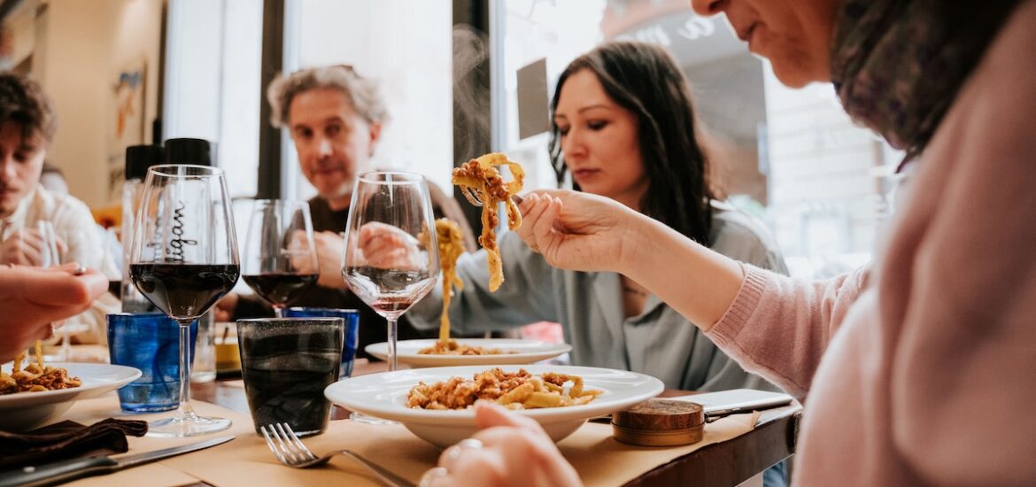 group of people seated at table enjoying plates of pasta and wine