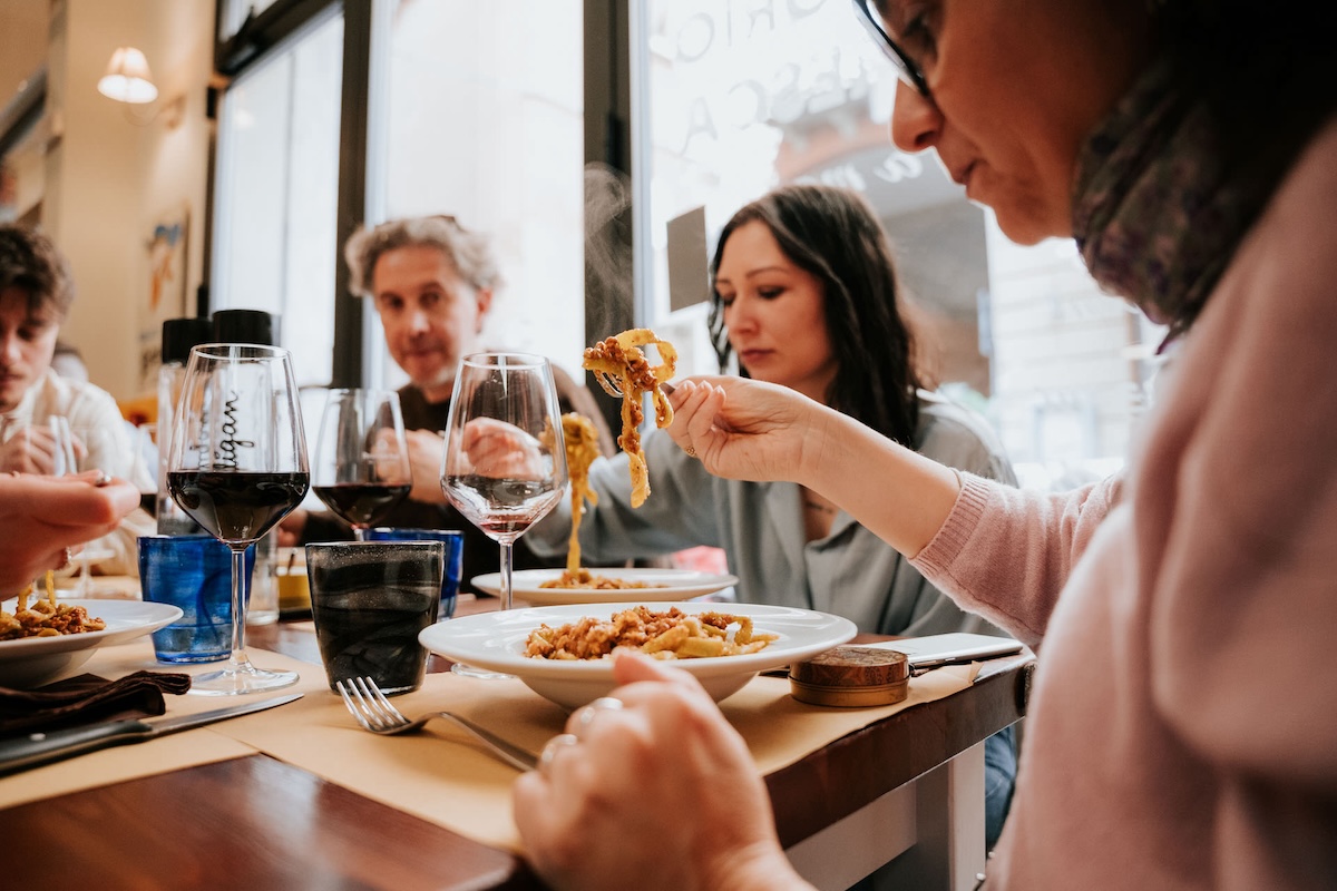 group of people seated at table enjoying plates of pasta and wine