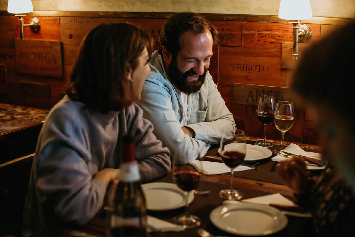 People eating at restaurants in Sintra at a table with ceramic plates and glasses of wine. 