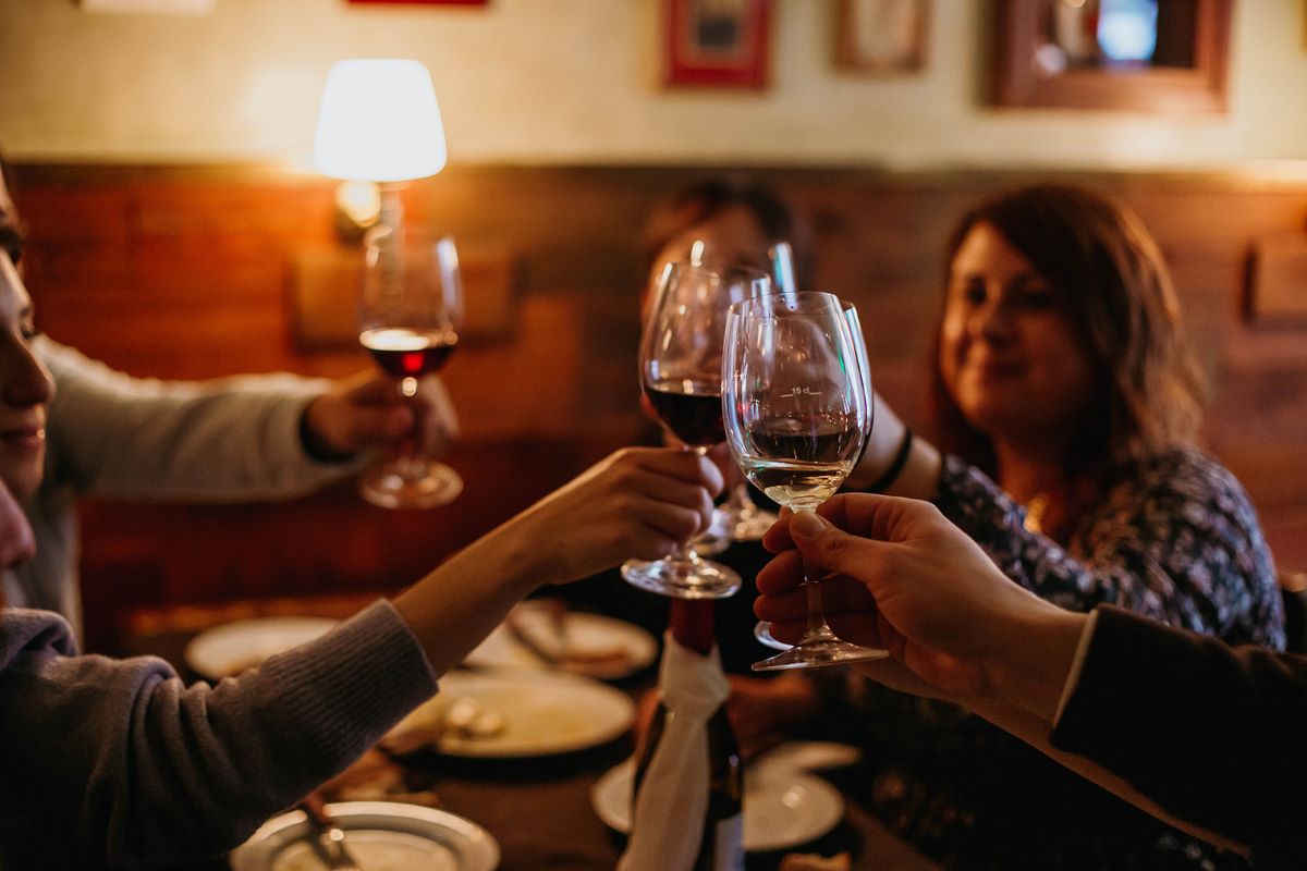 People at a restaurant cheering wine glasses with red and white wine .