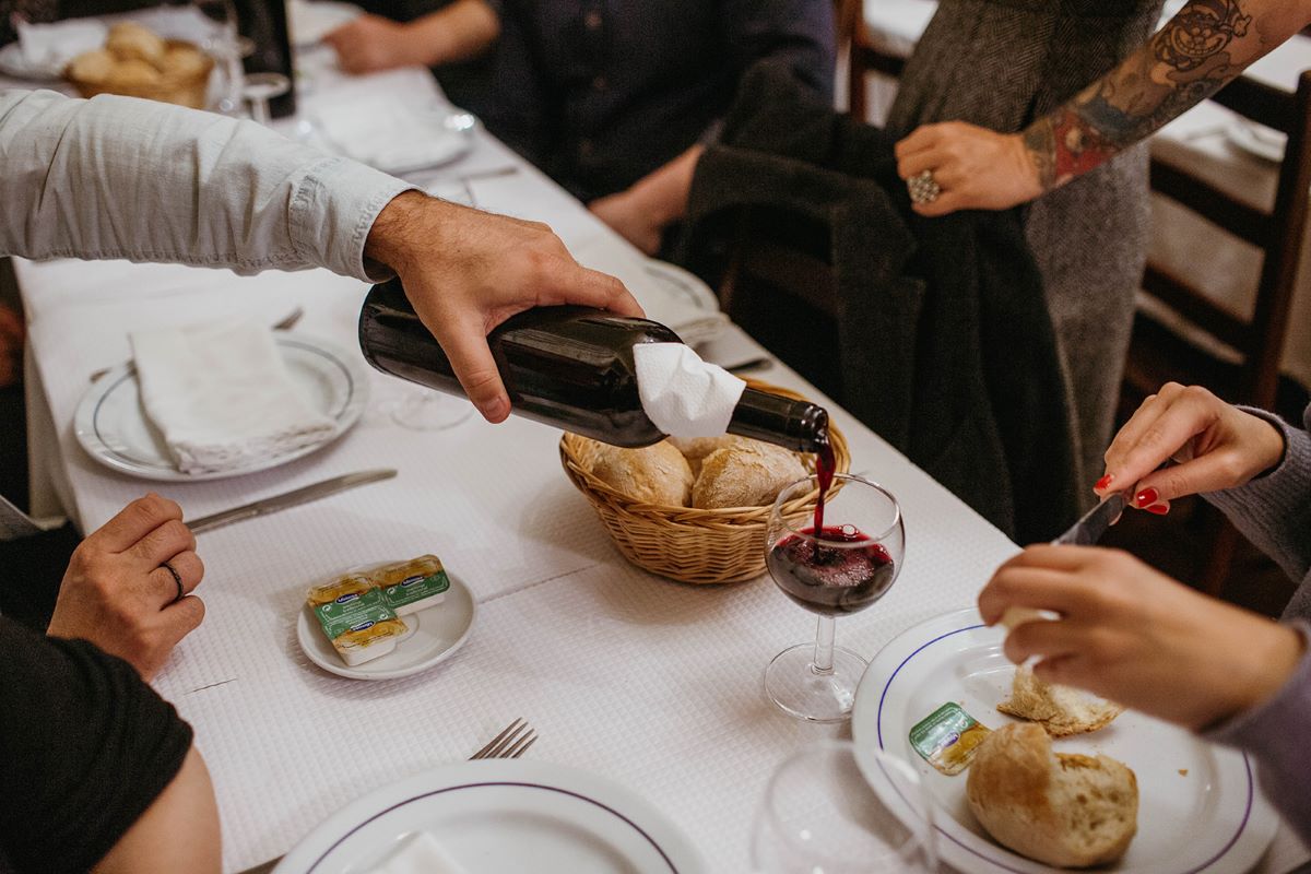 A man pouring a woman a glass of Portuguese wine while she butters her bread roll.