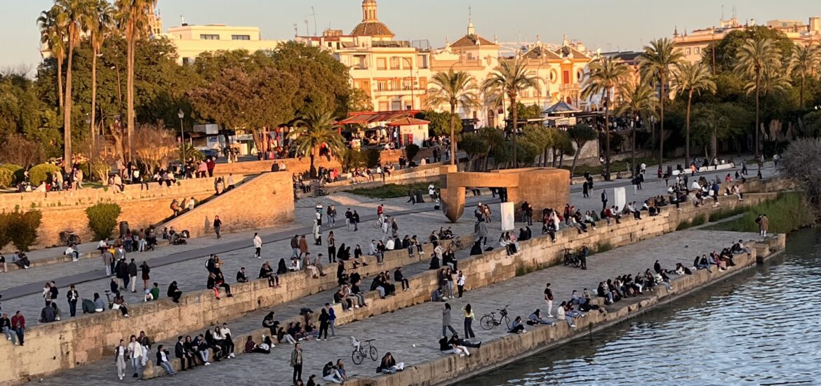 A group of people sitting near the river in Seville