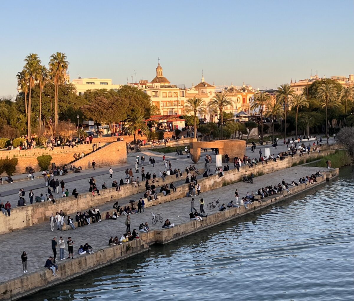 A group of people sitting near the river in Seville 