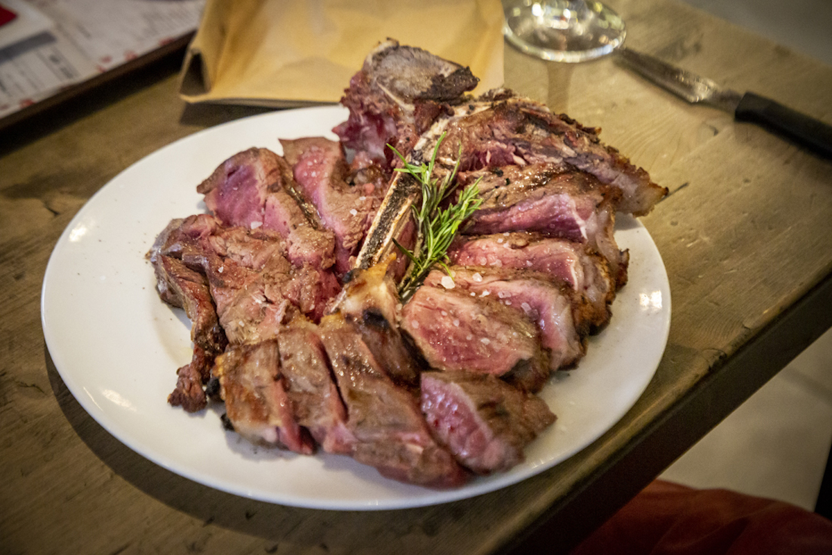 Close up of Florentine steak garnished with herbs and sprinkled with sea salt on a white plate