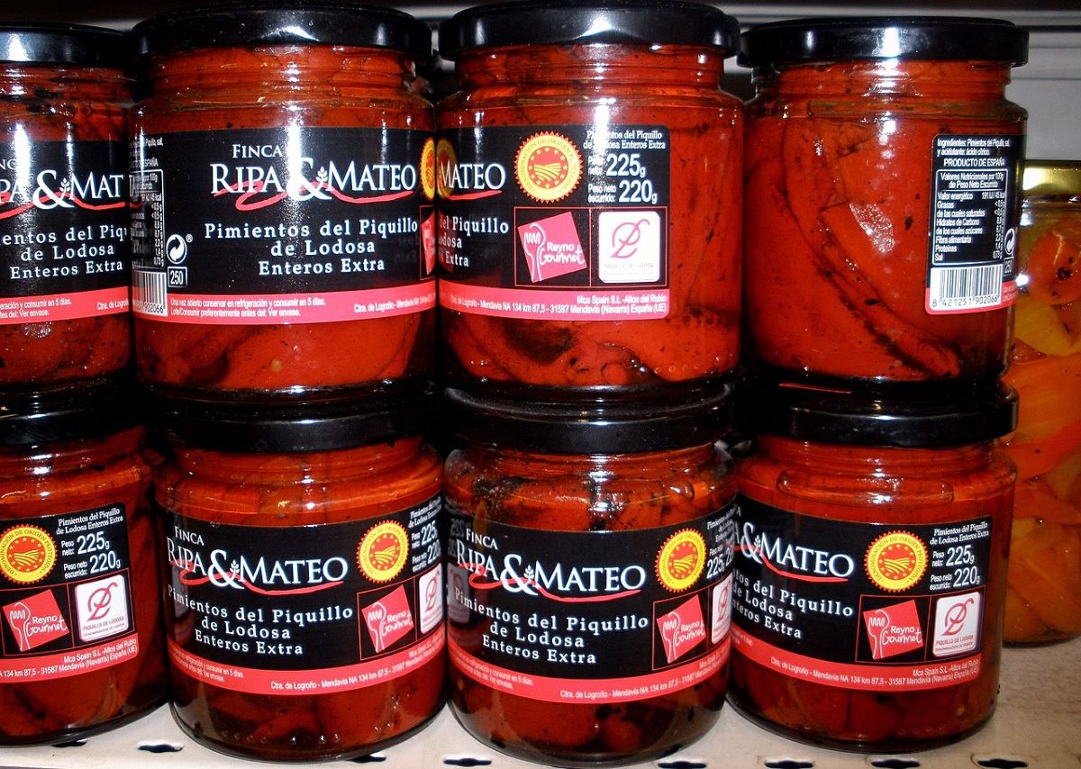 A row of Spanish piquillo peppers on a shelf at a grocery store which all display Denomination of Origin seals in Spain.