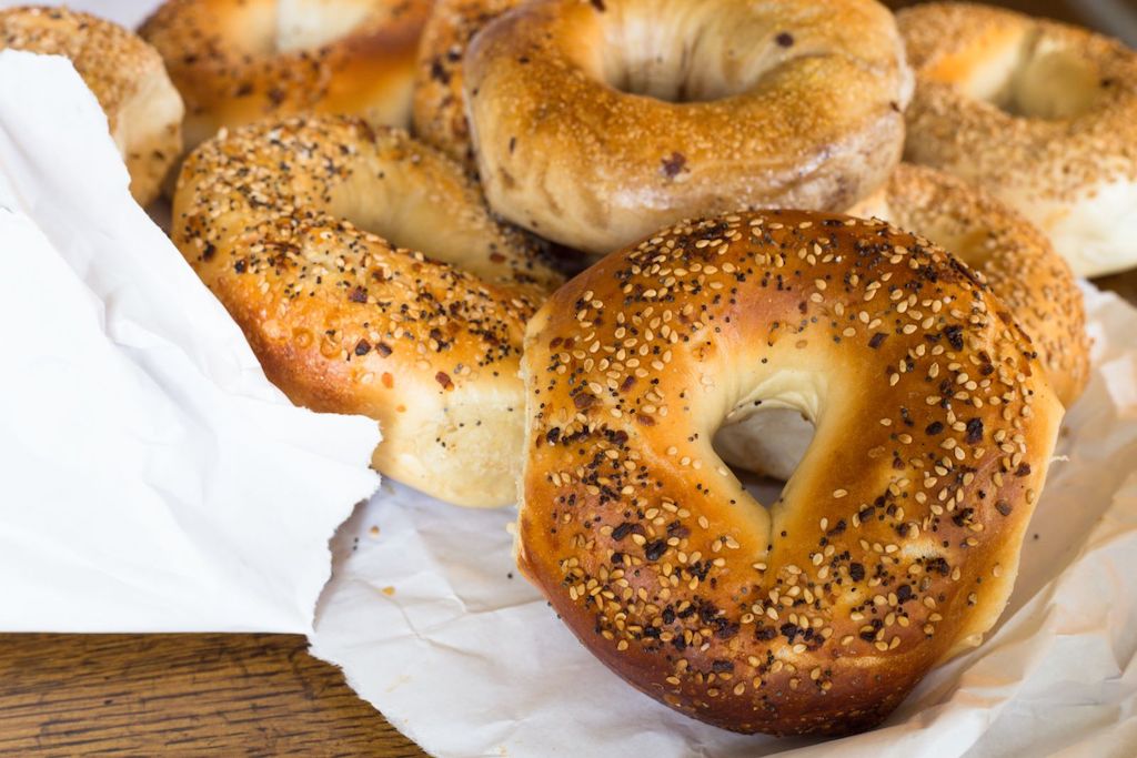 several bagels on a white paper bag with poppy and sesame seeds on top