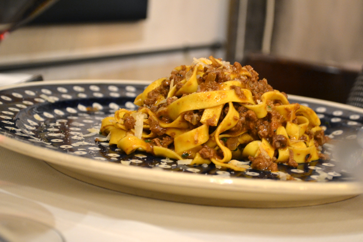 Wide pasta noodles served with boar ragu on a blue and white plate