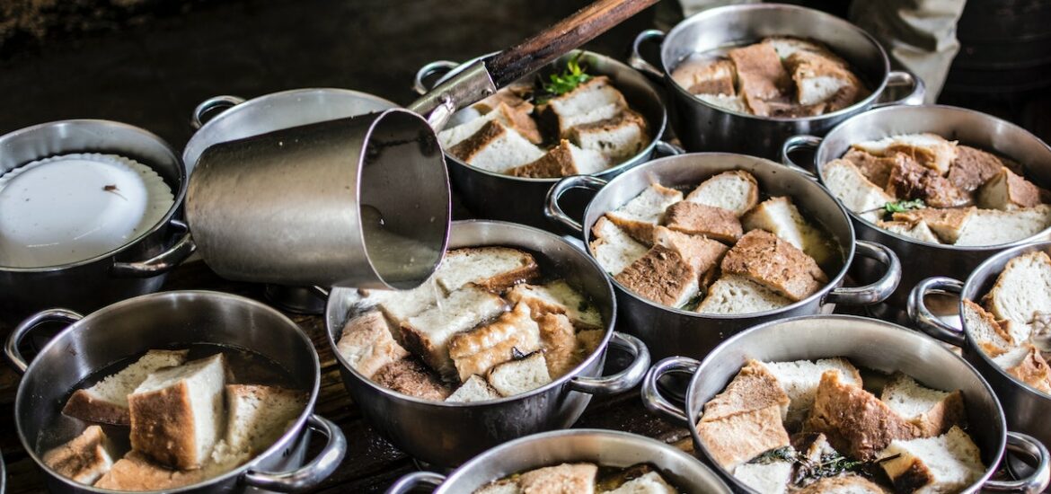 Several pots of garlic soup with bread chunks simmering on a stove