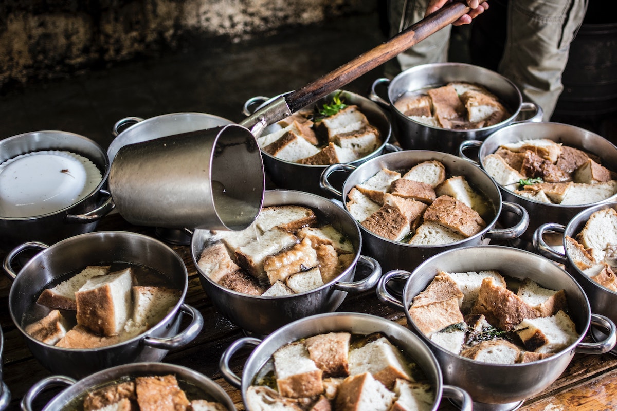 Several pots of garlic soup with bread chunks simmering on a stove