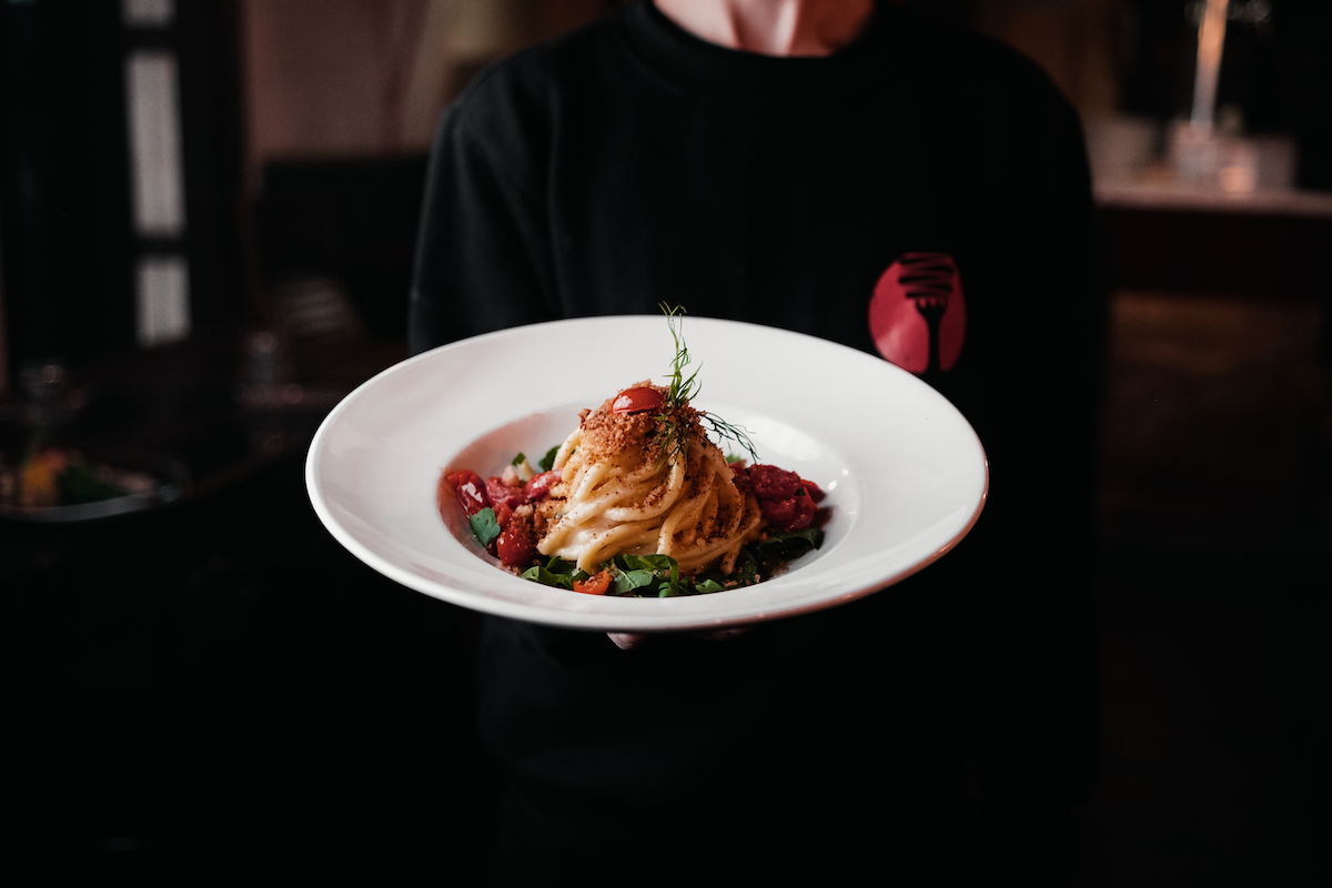 Pasta with tomato artfully presented on a white plate.