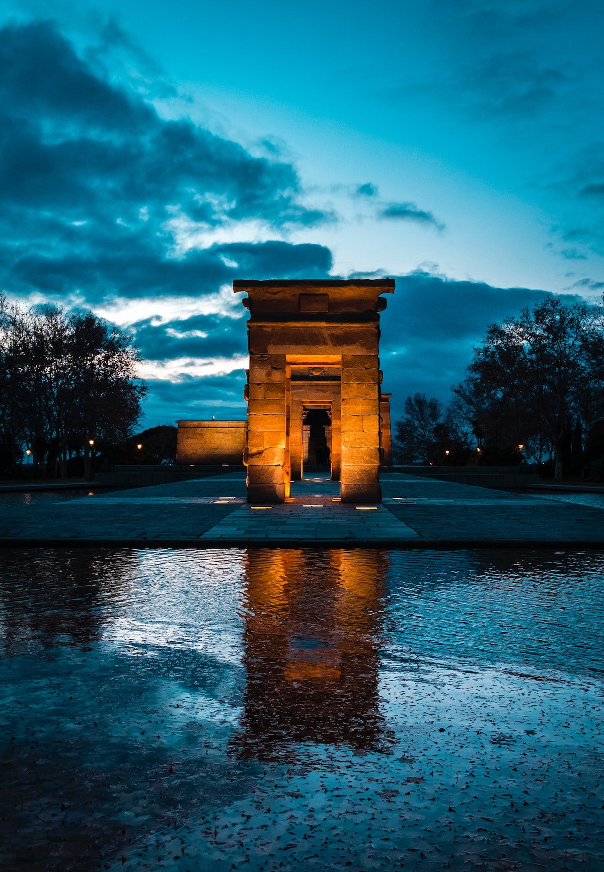 Nighttime view of the stone gateway of an Ancient Egyptian temple with a body of water in the foreground.